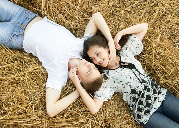 Šťastný mladý pár leží v oblasti slámy, pšenice na večer, romantické lidí koncepce, krásnou krajinu, letní sezóny — Stock fotografie