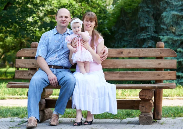 Retrato da família feliz no exterior, grupo de povos da árvore sentam-se no banco de madeira no parque da cidade, estação do verão, criança e pai — Fotografia de Stock
