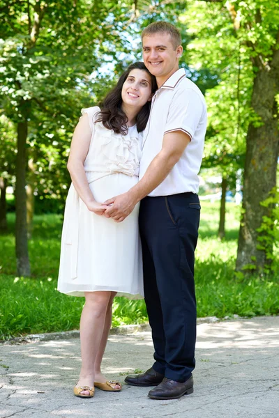 Gravid kvinna med man poserar i stadsparken, familjeporträtt, sommarsäsongen, grönt gräs och träd — Stockfoto