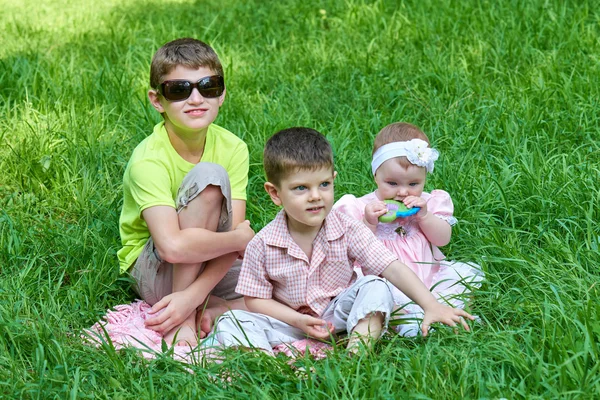 Tři děti sedí v trávě, hraní a zábava. — Stock fotografie