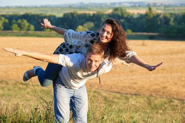 Lyckliga par att ha kul på utomhus, flicka rider på man tillbaka och fly - romantisk resa och människor koncept, sommar landskap med wheaten fält — Stockfoto