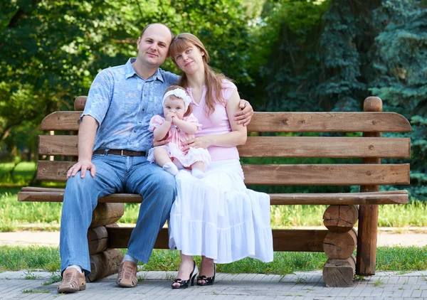 Retrato de família feliz com bebê menina ao ar livre, sente-se no banco de madeira no parque da cidade, temporada de verão, criança e pai — Fotografia de Stock
