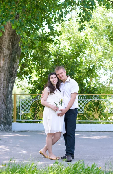 Zwangere vrouw met echtgenoot poseren in het stadspark, familieportret, zomerseizoen, groen gras en bomen — Stockfoto