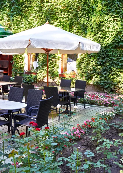 Café de calle interior con paraguas blanco, mesas y sillas, adornado con flores y hojas verdes — Foto de Stock