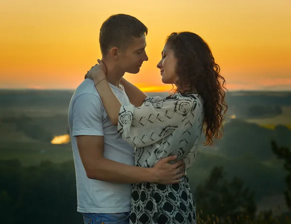 Casal romântico olhando uns para os outros ao pôr do sol ao ar livre, bela paisagem e céu amarelo brilhante, conceito de ternura amor, jovens adultos — Fotografia de Stock