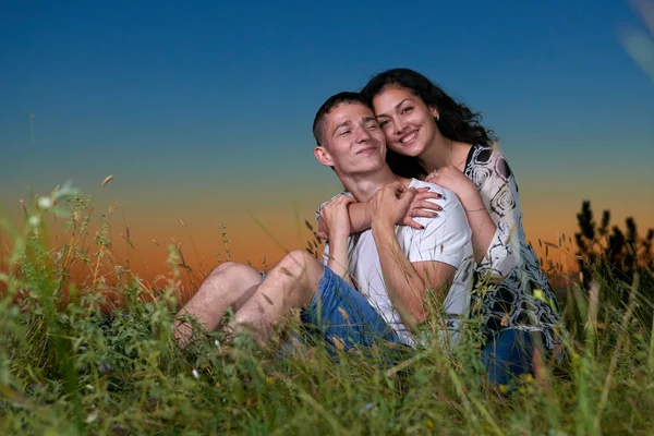 Romantisches Paar sitzt im Gras bei Sonnenuntergang im Freien, schöne Landschaft und dunkler Nachthimmel, Liebeskonzept, junge erwachsene Menschen — Stockfoto