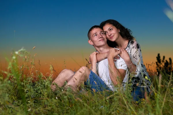 Romantische paar zitten op gras bij zonsondergang op outdoor, prachtige landschap en de donkere nachtelijke hemel hemel, liefde tederheid concept, volwassen jongeren — Stockfoto