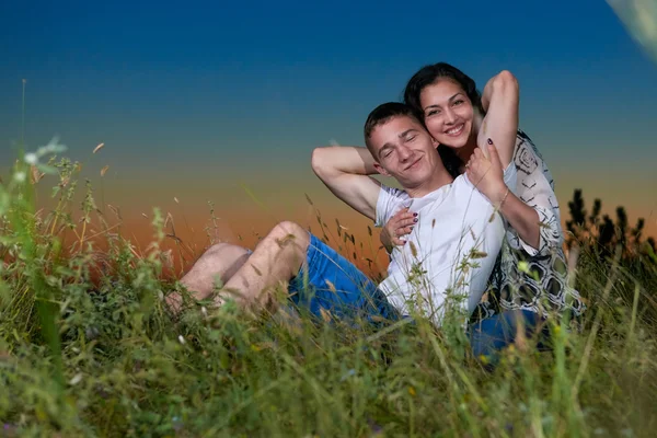 Romantische paar zitten op gras bij zonsondergang op outdoor, prachtige landschap en de donkere nachtelijke hemel, liefde concept, volwassen jongeren — Stockfoto