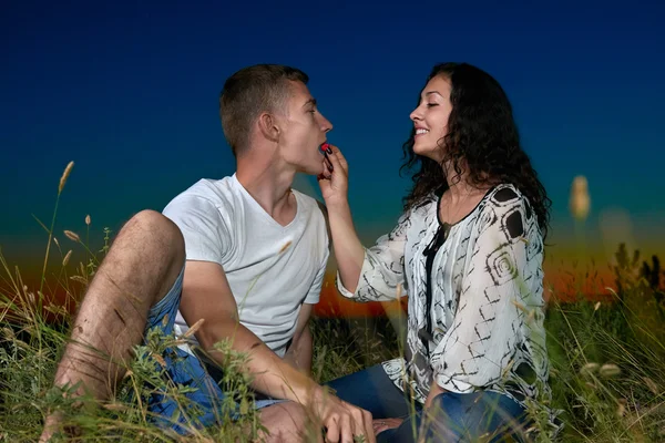 Para jeść czerwonej maliny, siedzieć na trawie, w ciemną noc niebo zewnątrz, miłość koncepcja, romantyczny młodych osób dorosłych — Zdjęcie stockowe