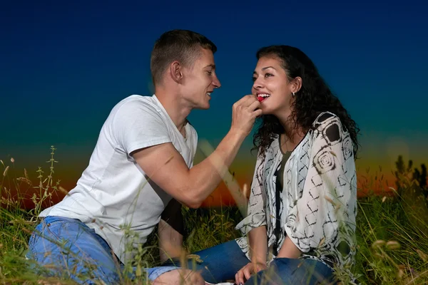 Пара їсть малину, сидить на траві на темному нічному небі на відкритому повітрі, концепція любові, романтичні молоді люди — стокове фото
