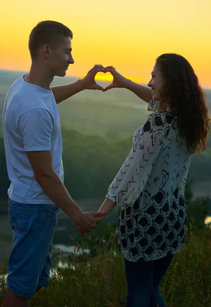 Романтична пара на заході сонця демонструє форму серця з рук, красивий пейзаж і яскраво-жовте небо, концепцію кохання ніжності, молодих дорослих людей — стокове фото