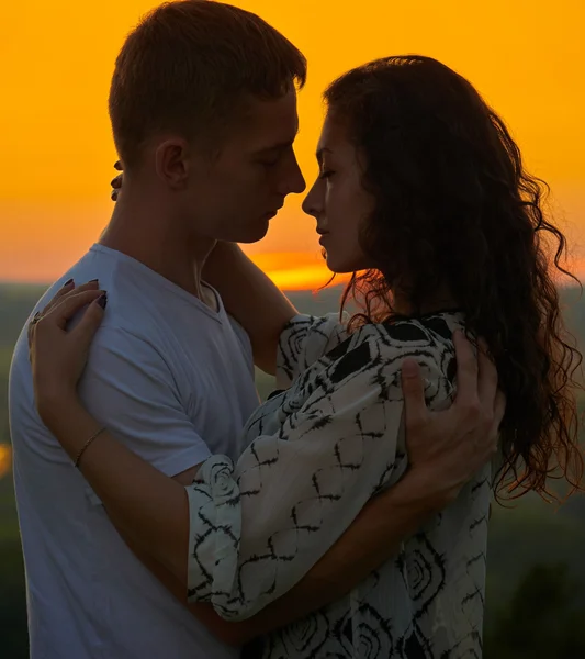Романтическая пара обнимают на закате на открытом воздухе, красивый пейзаж и ярко-желтое небо, любовь нежность концепции, молодые взрослые люди — стоковое фото