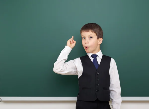 Estudante da escola menino posando no quadro-negro limpo, mostrar o dedo para cima e apontar, sorrir e emoções, vestido com um terno preto, conceito de educação, foto de estúdio — Fotografia de Stock