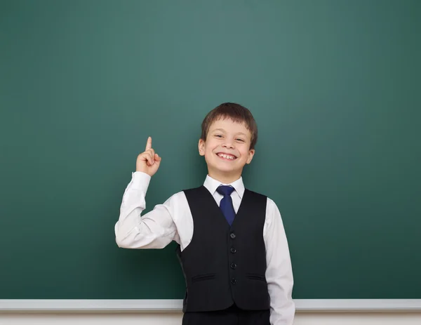 Estudante da escola menino posando no quadro-negro limpo, mostrar o dedo para cima e apontar, sorrir e emoções, vestido com um terno preto, conceito de educação, foto de estúdio — Fotografia de Stock