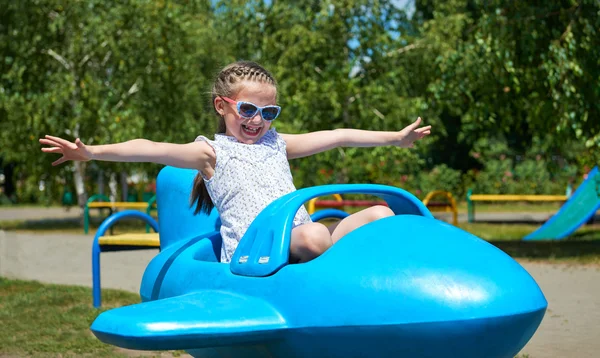 Niña volar en la atracción del avión azul en el parque de la ciudad, la infancia feliz, el concepto de vacaciones de verano —  Fotos de Stock