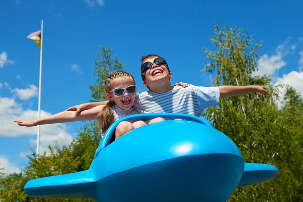 Niña y niño vuelan en atracción plano azul en el parque de la ciudad, infancia feliz, concepto de vacaciones de verano —  Fotos de Stock