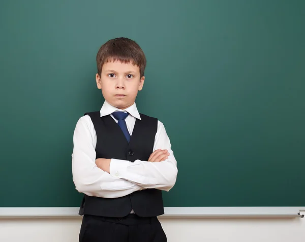 School student boy posing and think at the clean blackboard, grimacing and emotions, dressed in a black suit, education concept, studio photo — Stock Photo, Image