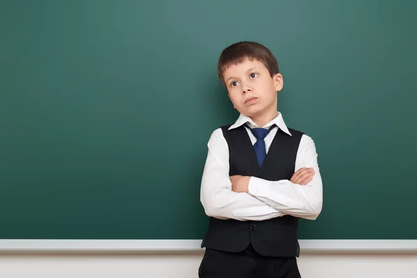 School student boy posing and think at the clean blackboard, grimacing and emotions, dressed in a black suit, education concept, studio photo — Stock Photo, Image