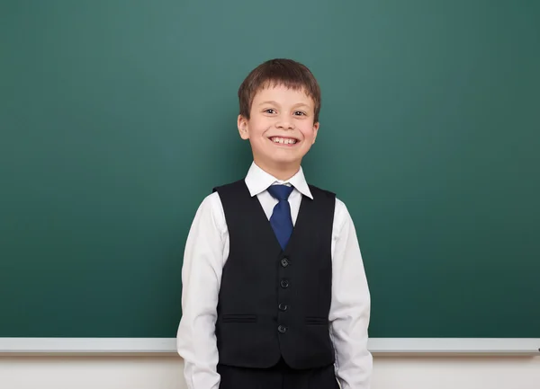 School student boy posing at the clean blackboard, grimacing and emotions, dressed in a black suit, education concept, studio photo — Stock Photo, Image