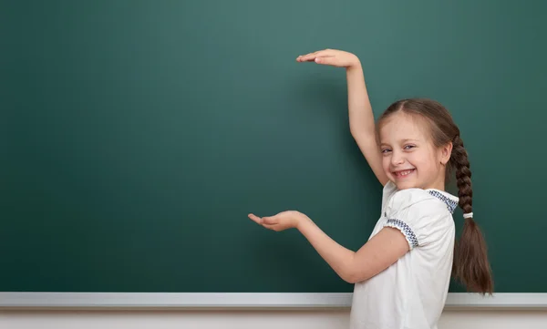 School student girl open arms at the clean blackboard, grimacing and emotions, dressed in a black suit, education concept, studio photo — Stock Photo, Image