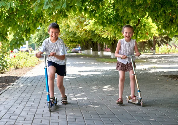Duas crianças passeio em scooters na calçada de rua na cidade ao ar livre, dia ensolarado brilhante — Fotografia de Stock
