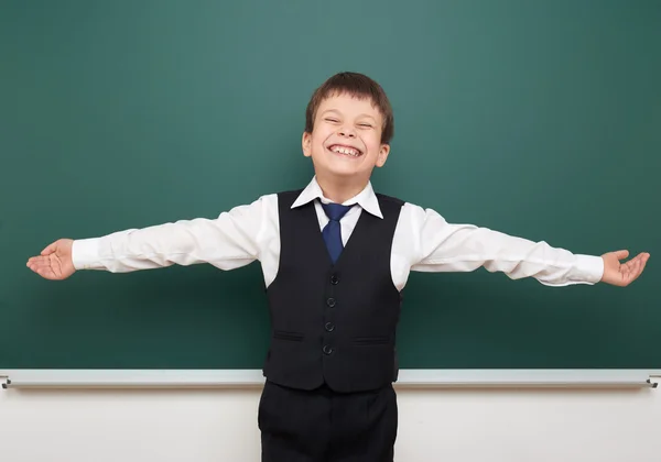 Studente ragazzo della scuola in posa alla lavagna pulita e braccia aperte, smorfie ed emozioni, vestito con un abito nero, concetto di educazione, foto di studio — Foto Stock