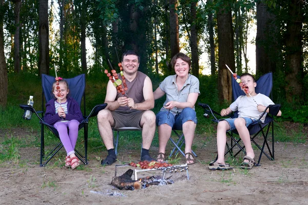Family in forest on picnic, make barbecue, meat cooked on fire, trees on background — Stock Photo, Image