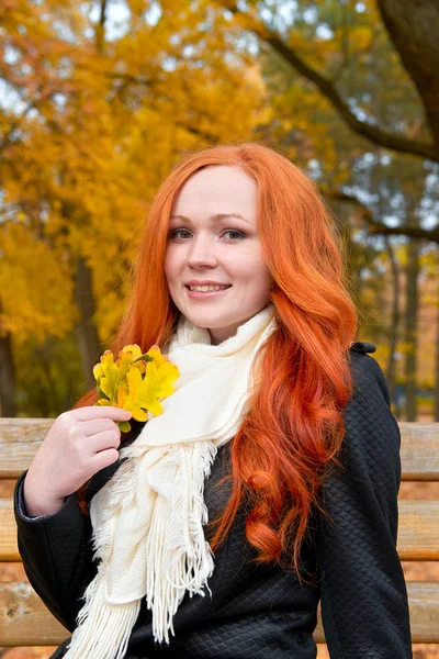 Bella ragazza ritratto sedersi su panchina in parco con foglia gialla in mano, stagione autunnale, rossa, capelli lunghi — Foto Stock