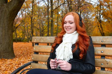 Kız Sonbahar sezonu dinle müzik kulaklık ile müzik çalar üzerinde oturup Şehir Parkı, sarı ağaçlar ve düşen yapraklar bankta