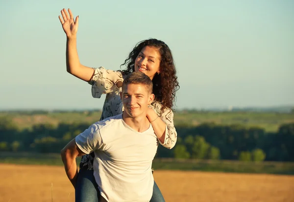 Feliz jovem casal andar no campo ao ar livre, conceito de pessoas românticas, temporada de verão, menina montando no homem de volta e acenando — Fotografia de Stock
