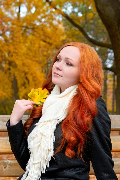 Bella ragazza ritratto sedersi su panchina in parco con foglia gialla in mano, stagione autunnale, rossa, capelli lunghi — Foto Stock