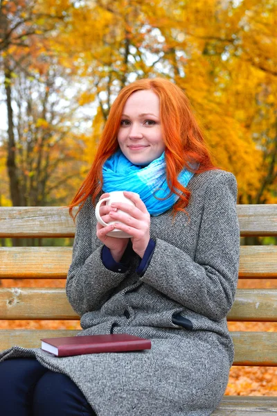 Retrato menina com copo e livro em folhas amarelas fundo, época de outono — Fotografia de Stock