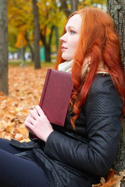 kitap kızla oturup sonbahar ormandaki sarı yapraklarda