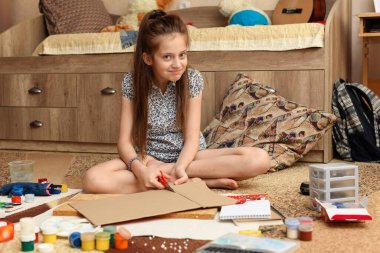 Kız evde resim çiziyor, sanat eseri yapıyor, kağıt, boya ve fırçalardan yaratıcı sanat eserleri yapıyor.