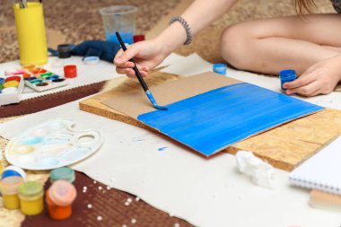 Kız evde resim çiziyor, sanat eseri yapıyor, kağıt, boya ve fırçalardan yaratıcı sanat eserleri yapıyor.