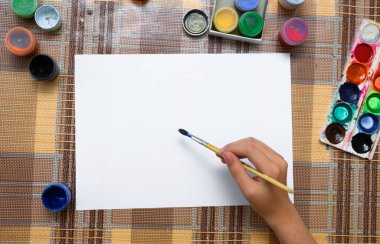 Beyaz bir kağıda suluboya çizen bir kız evde sanatsal bir eser yaratıyor.