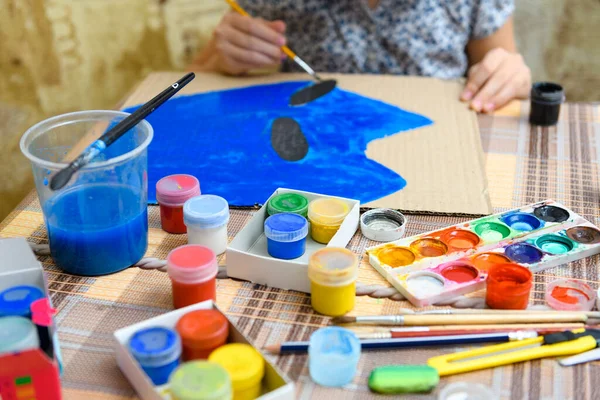 青いガッシュの段ボールを描く少女は家で創造的なアートワークを作り — ストック写真