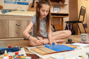 Kız evde resim çiziyor, sanat eseri yapıyor, kağıt, boya ve fırçalardan yaratıcı sanat eserleri yapıyor.