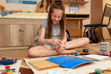 Kız evde resim çiziyor, sanat eseri yapıyor, kağıt, boya ve fırçalardan yaratıcı sanat eserleri yapıyor.