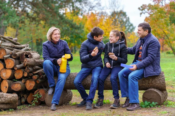 family relaxing outdoor in autumn city park, happy people together, parents and children, they drink tea and eat sandwiches, talking and smiling, beautiful nature