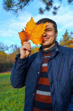 Sonbahar parkında poz veren bir adamın portresi, arka plan olarak parlak renkli yapraklar.