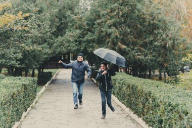 Baba ve kızı şemsiyeyle koşuyor, Autumn City Caddesi, mutlu insanlar birlikte, ebeveynler ve çocuklar