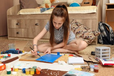 Kız evde resim çiziyor, sanat eseri yapıyor, kağıt, boya ve fırçalardan yaratıcı sanat eserleri yapıyor.
