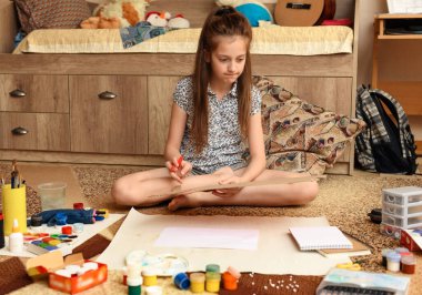 Kız evde resim çiziyor, sanat eseri yapıyor, kağıt, boya ve fırçalardan yaratıcı sanat eserleri yapıyor.