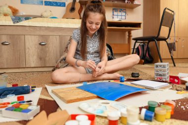 Kız evde resim çiziyor, sanat eseri yapıyor, kağıt, boya ve fırçalardan yaratıcı sanat eserleri yapıyor.