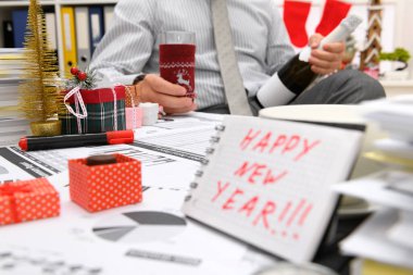 İş ve tatil konsepti - işadamı ofiste Noel ağacı, şeker ve diğer yeni yıl süslemeleri ile süslenmiş kutluyor. Mutlu yeni yıl metni içeren bir not defteri gösterirName