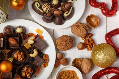 Noel ya da tatil süslemeleri için tatlı yemek arkaplanı - çikolata şekerlemeleri, mandalinalar, fındıklar ve kuru meyveler beyaz ahşap üzerinde