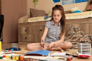 Kız evde resim çiziyor, sanat eseri yapıyor, kağıt, boya ve fırçalardan yaratıcı sanat eserleri yapıyor.