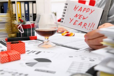 İş ve tatil konsepti - işadamı ofiste Noel ağacı, şeker ve diğer yeni yıl süslemeleri ile süslenmiş kutluyor. Mutlu yeni yıl metni içeren bir not defteri gösterirName