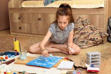 Kız evde resim çiziyor, sanat eseri yapıyor, kağıt, boya ve fırçalardan yaratıcı sanat eserleri yapıyor.